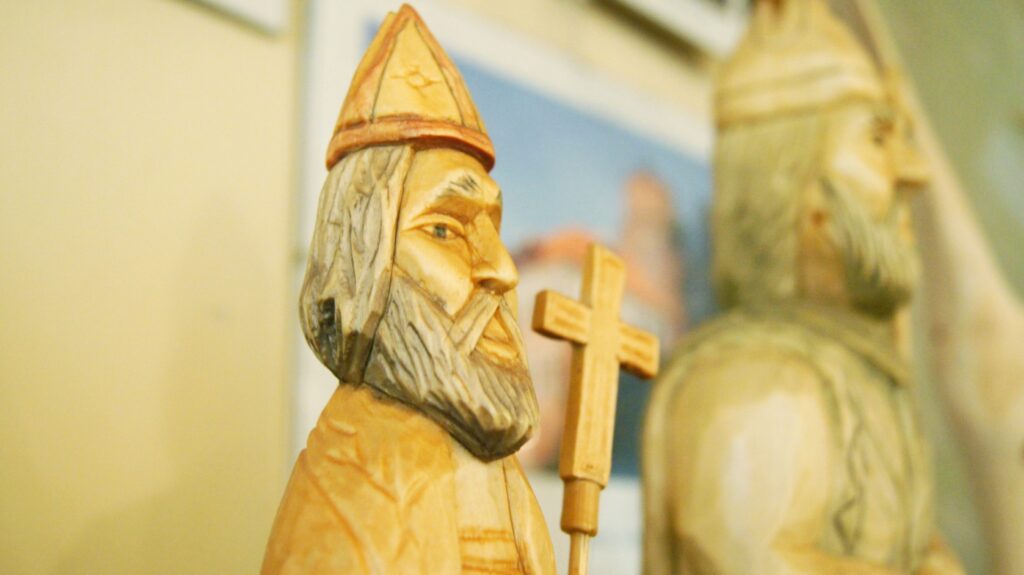Drewniana rzeźba. Postać mężczyzny z brodą, wąsami, w rękach trzyma drewniany krzyż
