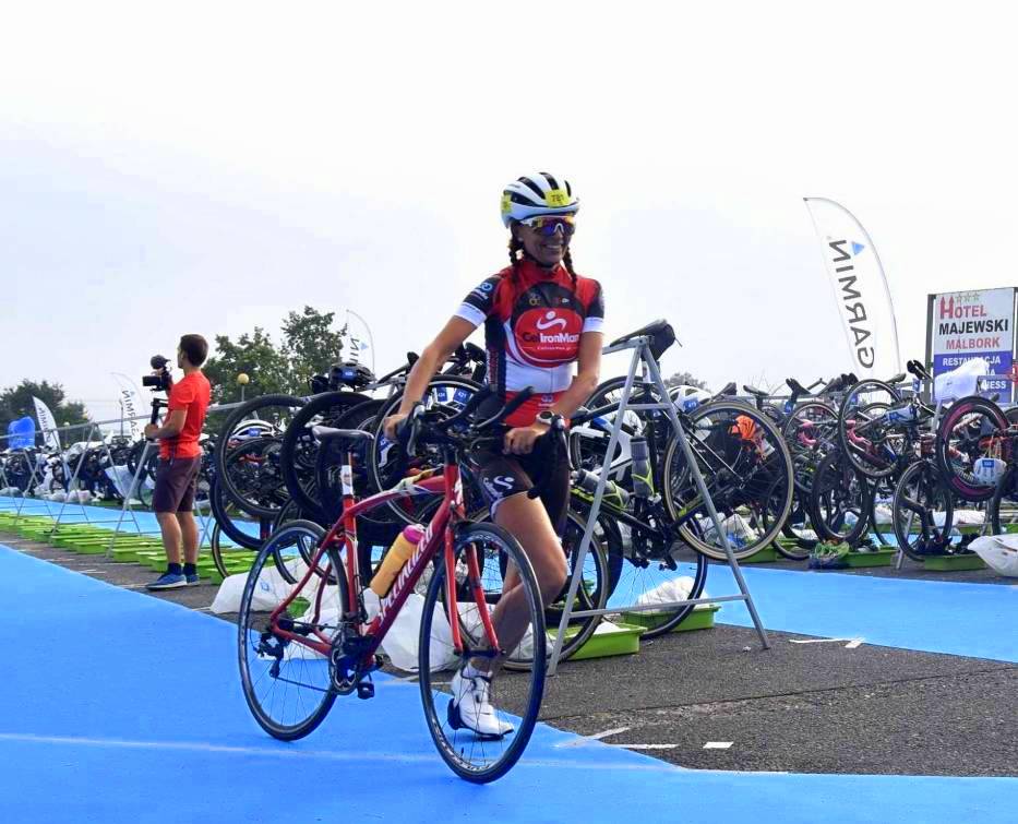 Kobieta podczas zawodów triathlonowych. Prowadzi rower